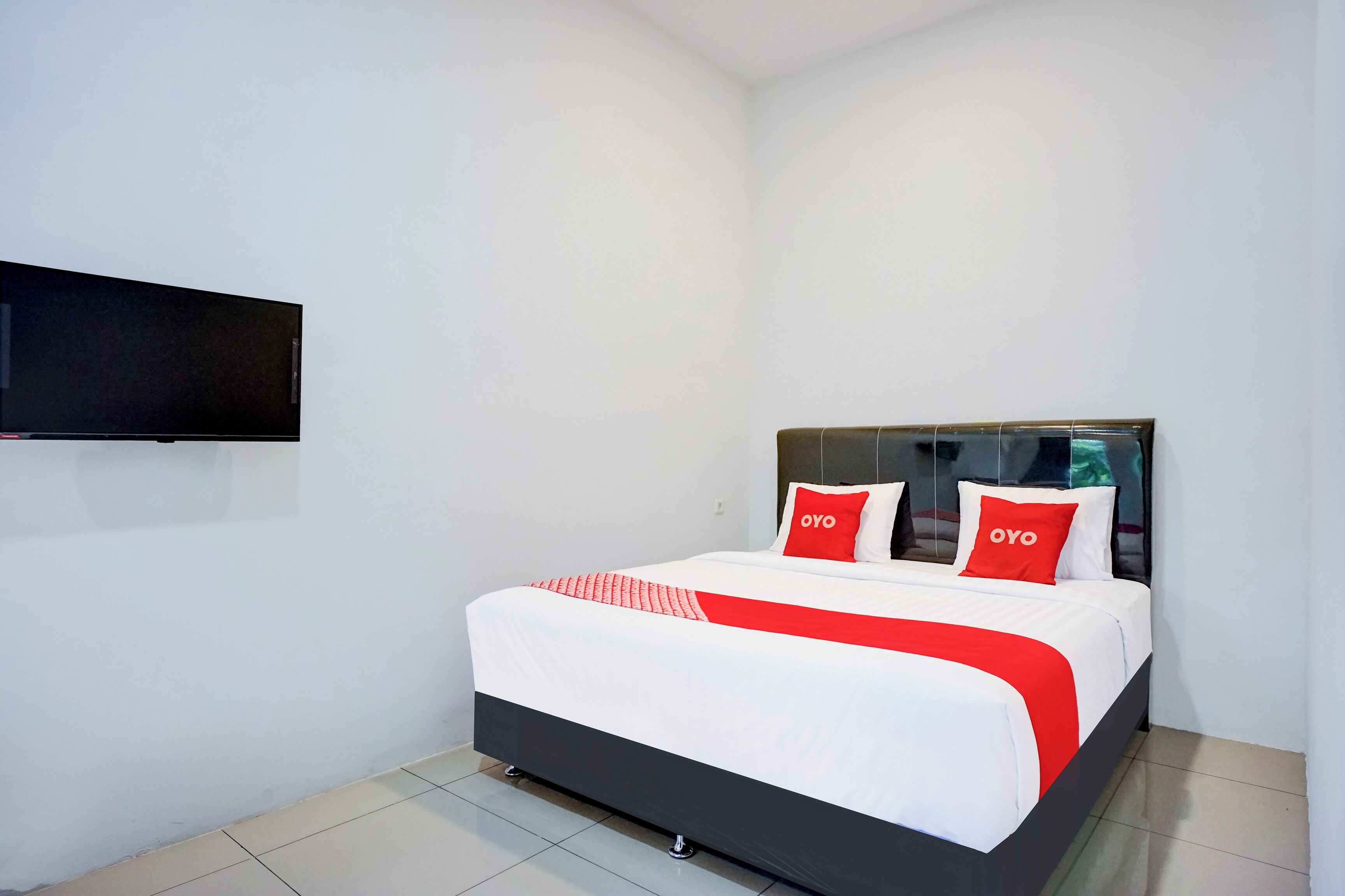 A modern hotel room with a large bed, white walls, and a flat-screen TV mounted on the wall.