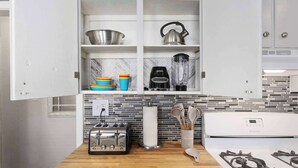 Eine moderne Küche mit weißen Schränken, einer Holz Arbeitsplatte, einem Gasherd, einem Toaster, einem Mixer und bunten Schüsseln.