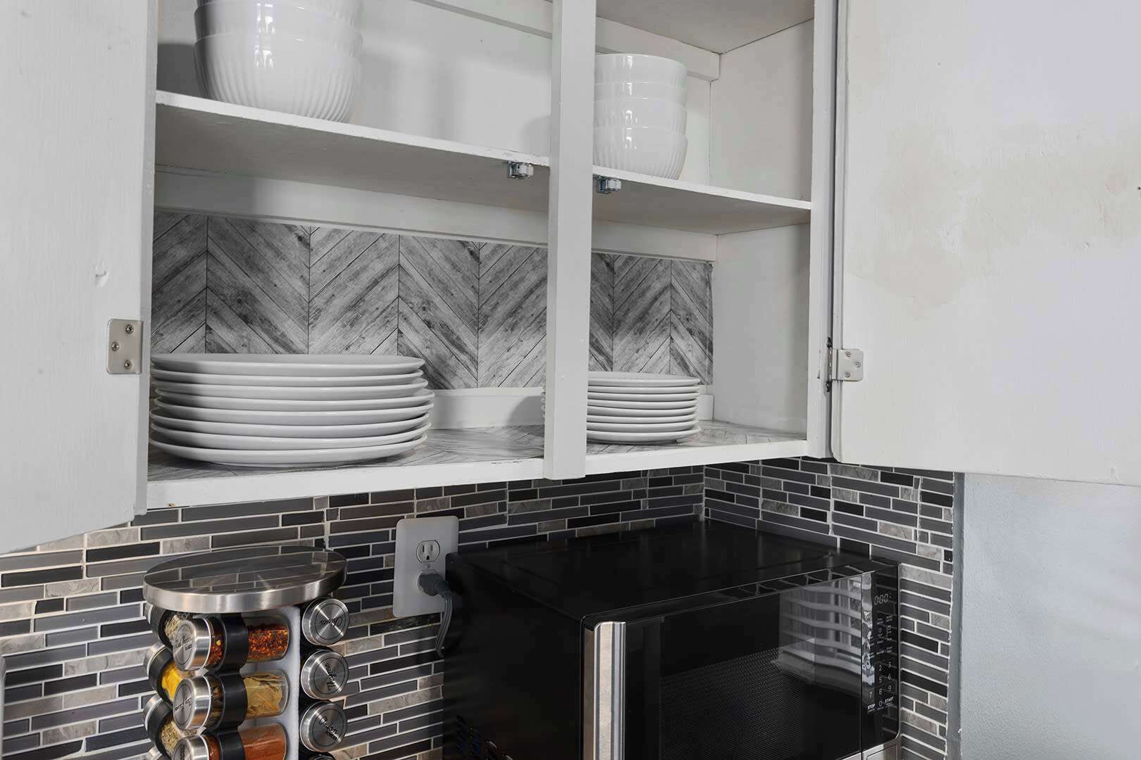 Een keuken met witte kasten, een zwart fornuis en een backsplash van visgraatmozaïek.