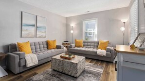 Ein modernes Wohnzimmer mit zwei grauen Sofas, gelben Kissen, einem Couchtisch und einem Bücherregal.
