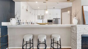 A modern kitchen with white cabinets, a central island with stools, and pendant lighting. - Beautiful Home_Large Space_3 BR_HotTub_Deck (Houston)