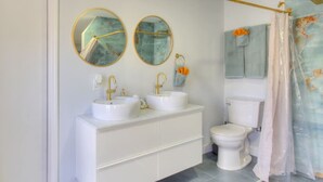 Casa de banho com duas pias, sanita e cortina de chuveiro.