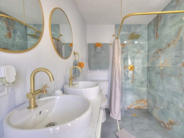 A bathroom with two sinks, a shower, and marble walls.