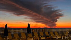 Vista do pôr do sol a partir de uma varanda, com fileiras de espreguiçadeiras e guarda-sóis.