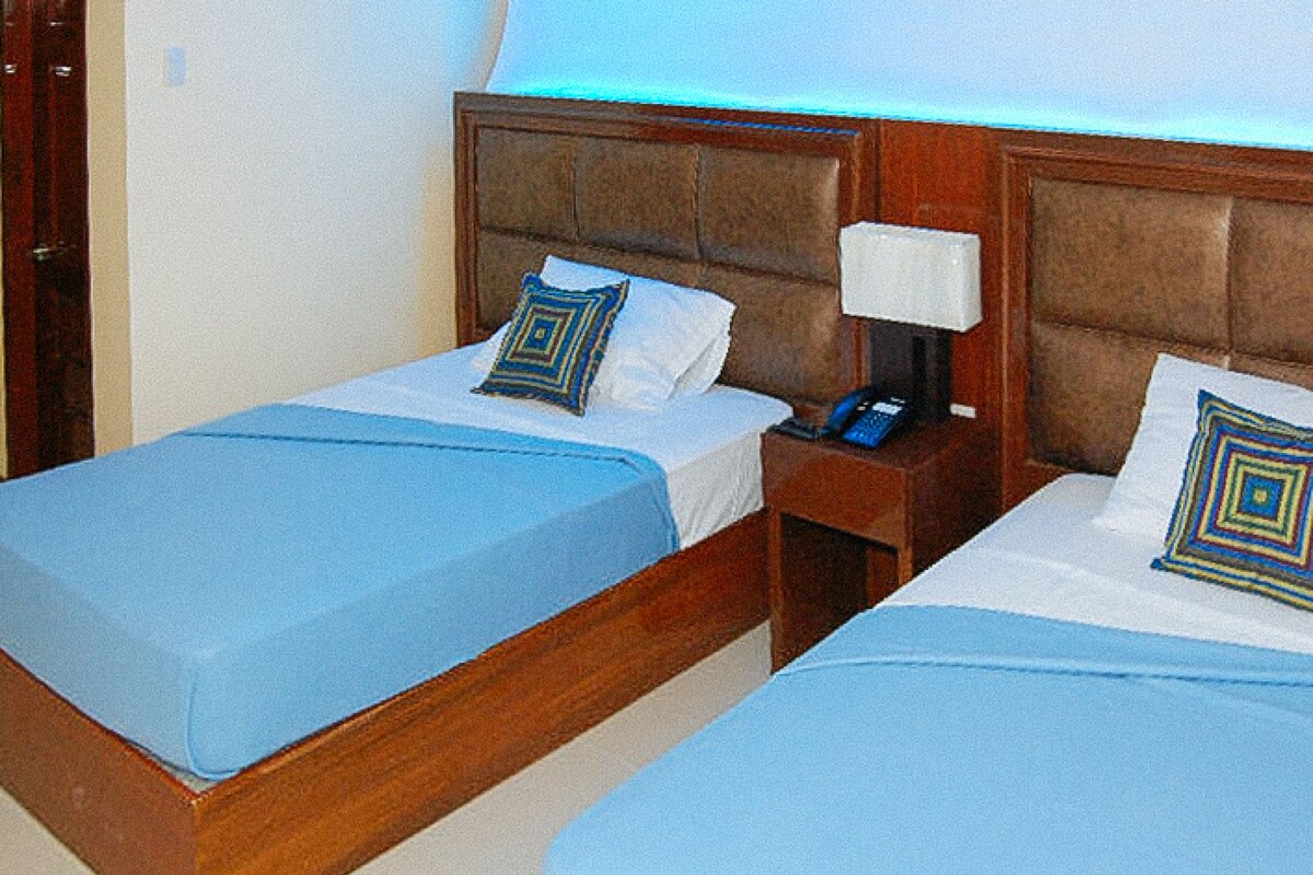 Two adjacent beds with blue bedding, wooden headboards, and bedside lamps.