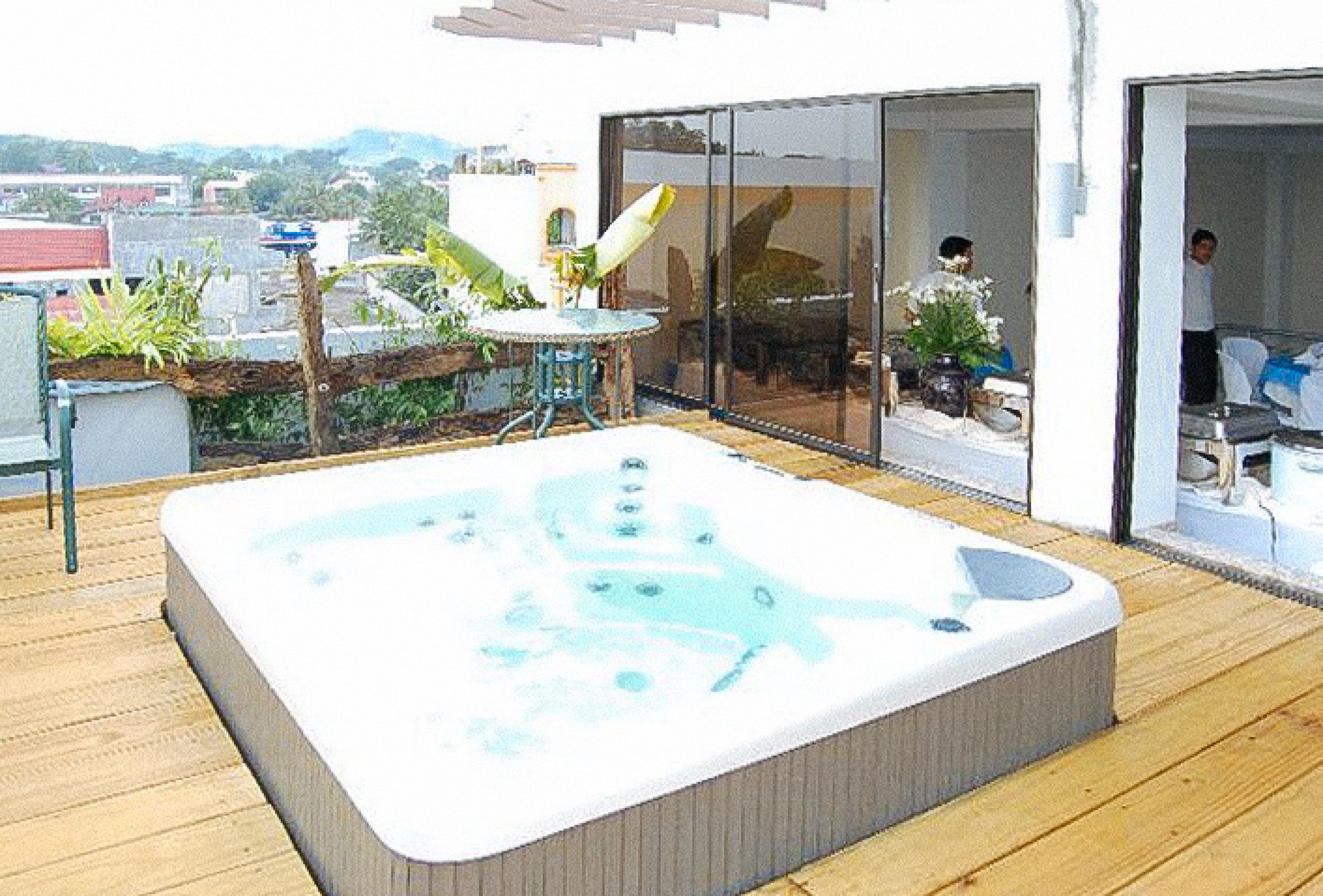 Un jacuzzi en una terraza de madera con un ventanal que da a una habitación.