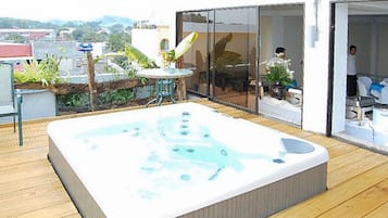 Un jacuzzi en una terraza de madera con un ventanal que da a una habitación.