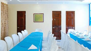A conference room with a long table covered in blue, surrounded by white chairs. There are three wooden doors and a framed picture on the wall.