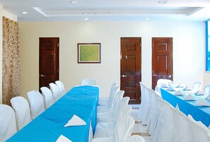 A conference room with a long table covered in blue, surrounded by white chairs. There are three wooden doors and a framed picture on the wall. - Sky Garden Hotel By Reddoorz (Roxas City)