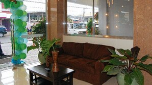 A room with a brown sofa, a small table, and potted plants. - Sky Garden Hotel By Reddoorz (Roxas City)