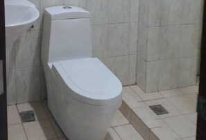 A bathroom with a toilet, sink, and tiled floor. - Sky Garden Hotel By Reddoorz (Roxas City)