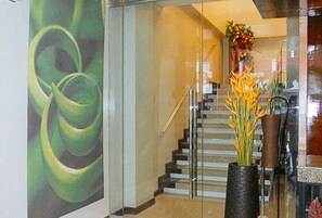 A staircase with a glass railing, a vase with yellow flowers, and a green abstract painting on the wall. - Sky Garden Hotel By Reddoorz (Roxas City)
