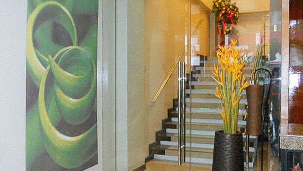 A staircase with a glass railing, a vase with yellow flowers, and a green abstract painting on the wall. - Sky Garden Hotel By Reddoorz (Roxas City)
