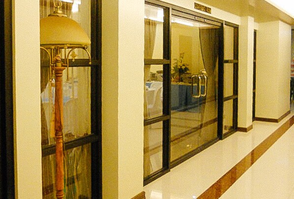 A hallway with a lamp, a glass door, and a table with chairs. - Sky Garden Hotel By Reddoorz (Roxas City)