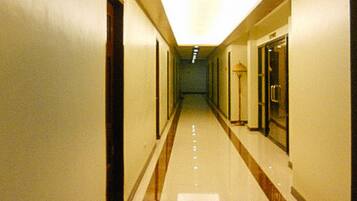 Corredor longo e estreito de hotel, com portas em ambos os lados e um caminho central.