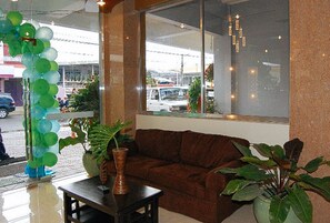 A room with a brown sofa, a small table, and potted plants. - Sky Garden Hotel By Reddoorz (Roxas City)