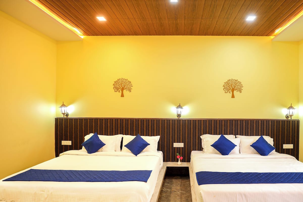 Habitación de hotel con dos camas, cabecera de madera panelada, paredes amarillas y diseños de árboles decorativos.