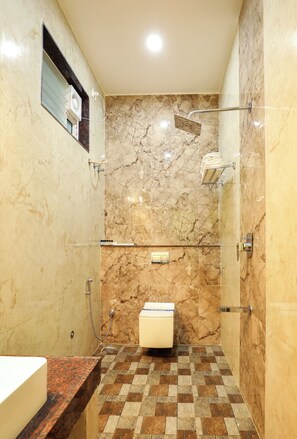 A bathroom with a marble wall, a glass shower enclosure, a tiled floor, and a toilet. - Coastal Grand Akshaya - Kothagiri (Ootacamund)