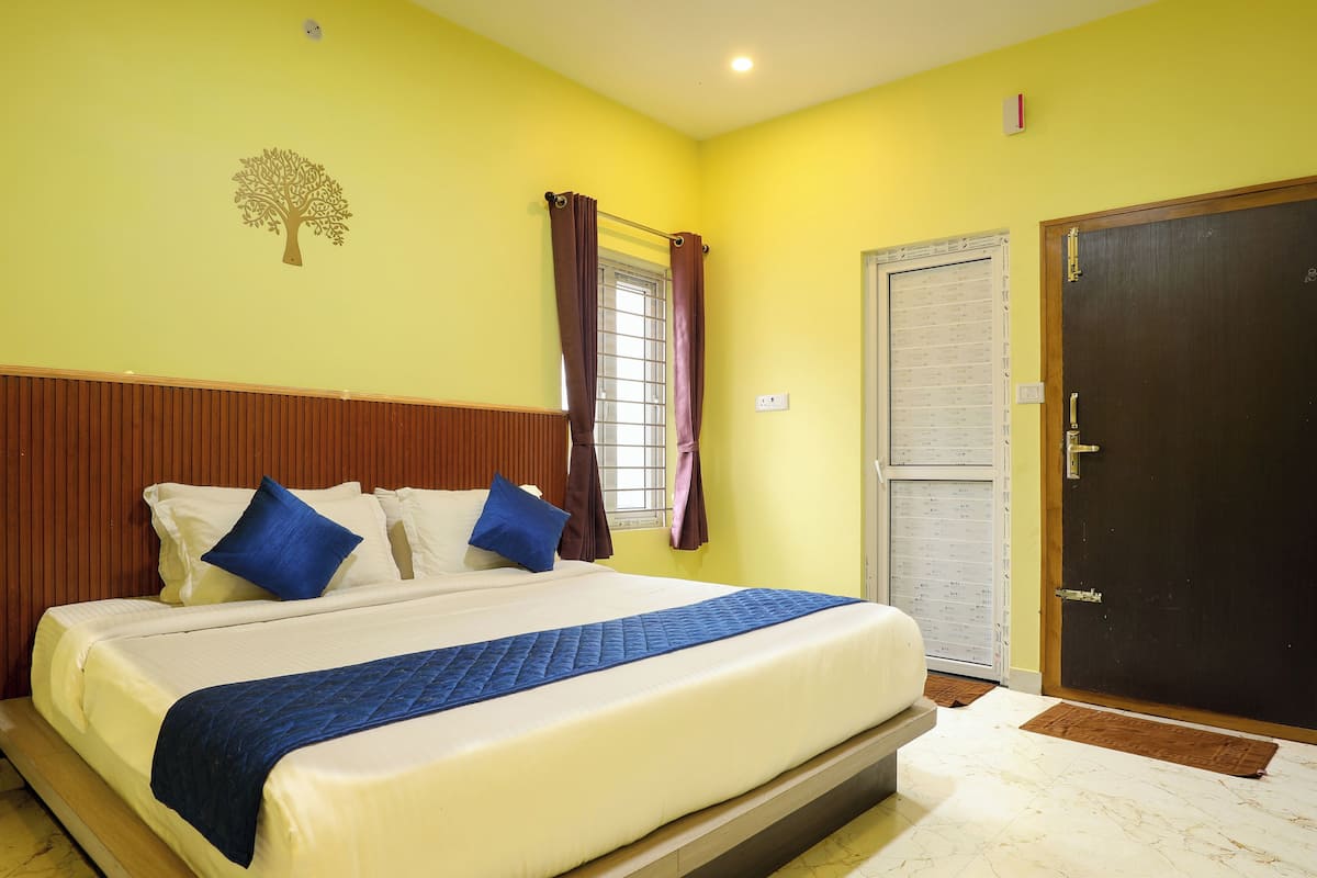 Habitación de hotel con una cama grande, cabecera de madera, una ventana con cortinas, una puerta y un aplique de pared.