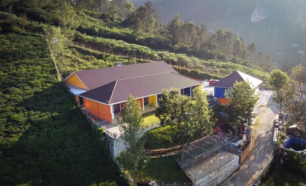 A two-story house with a tiled roof, surrounded by lush greenery and a hilly landscape. - Coastal Grand Akshaya - Kothagiri (Ootacamund)