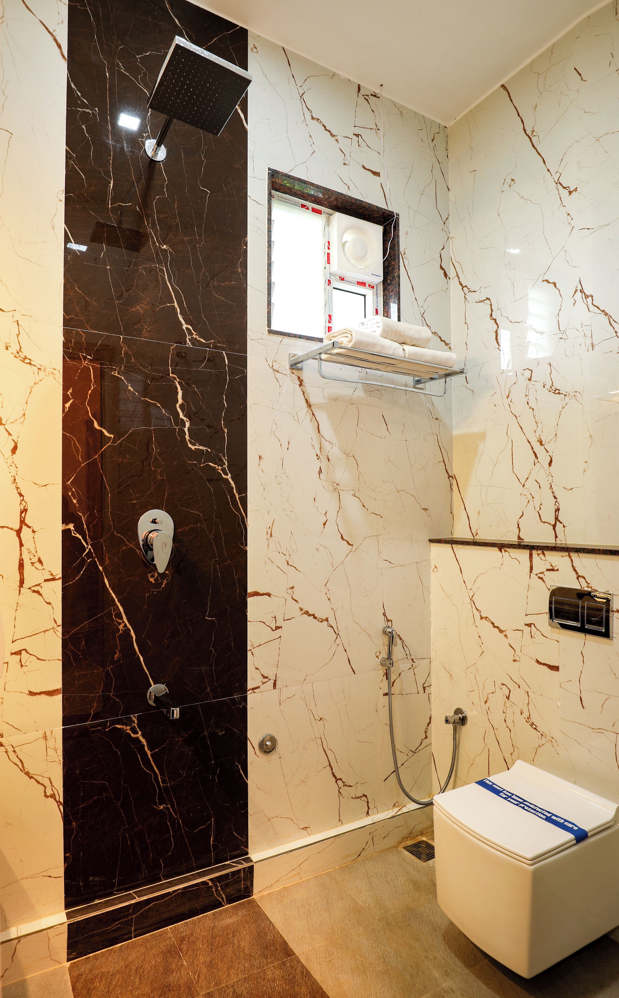 A bathroom with a black marble wall, a shower, a toilet, and a shelf with towels.