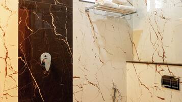 A bathroom with a black marble wall, a shower, a toilet, and a shelf with towels.