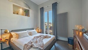 A modern bedroom with a large bed, a nightstand, a dresser, and a view of the city through a window. - Spacious 3-Bedroom Apartment with Stunning Rooftop Terraces in San Lorenzo
 (Firenze)
