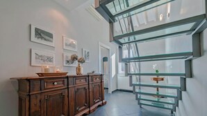 A modern interior with a wooden cabinet, framed pictures, and a glass staircase. - Spacious 3-Bedroom Apartment with Stunning Rooftop Terraces in San Lorenzo
 (Firenze)
