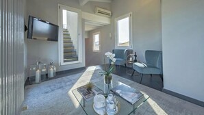A modern living room with a glass coffee table, a flat-screen TV mounted on the wall, and a staircase leading to another level. - Spacious 3-Bedroom Apartment with Stunning Rooftop Terraces in San Lorenzo
 (Firenze)