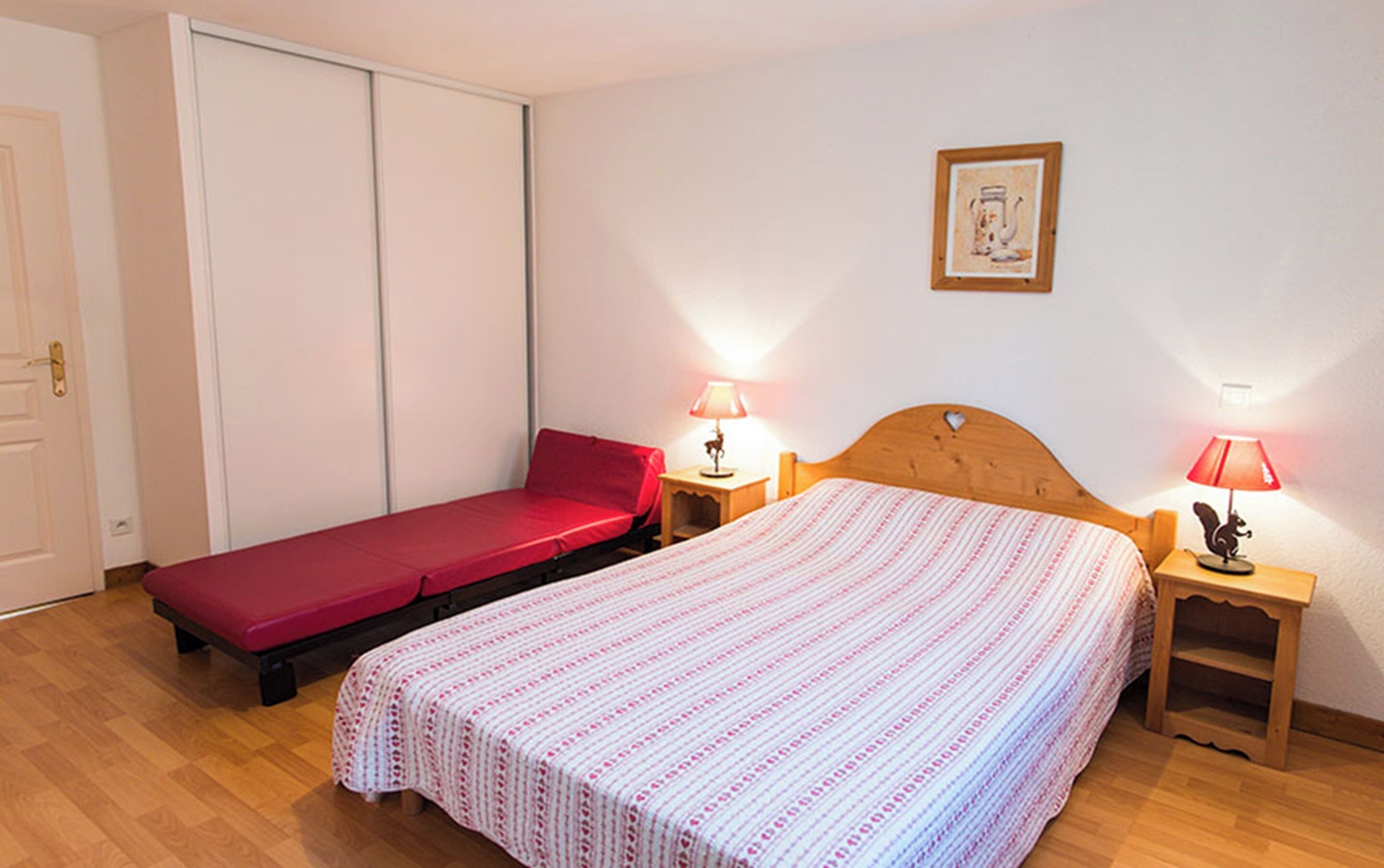 A room with two beds, a wardrobe, a framed picture on the wall, and two bedside lamps.