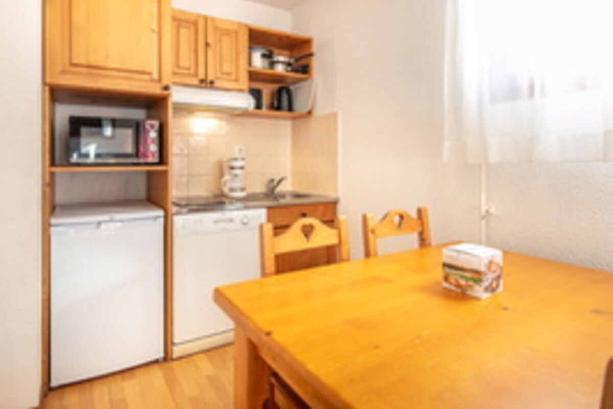 Una cocina compacta con armarios de madera, microondas, lavavajillas y una mesa de comedor con sillas.