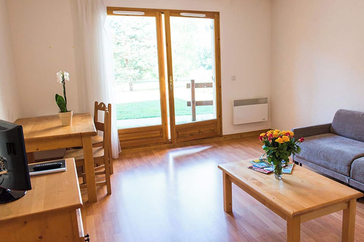 Un salon avec une table en bois, un canapé, un téléviseur et une fenêtre donnant sur un paysage verdoyant.