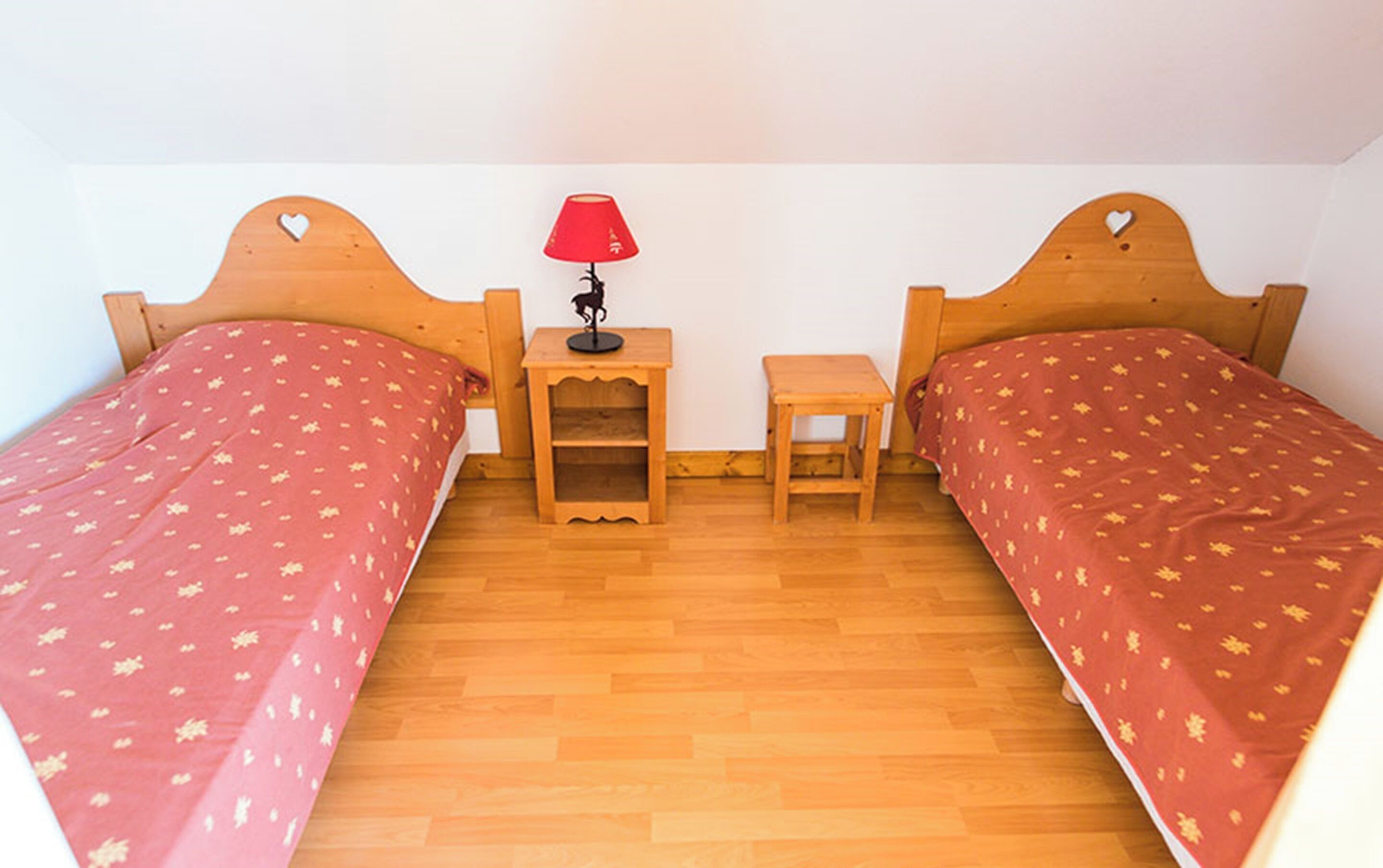 A room with two wooden beds, a small table with a lamp, and a nightstand.