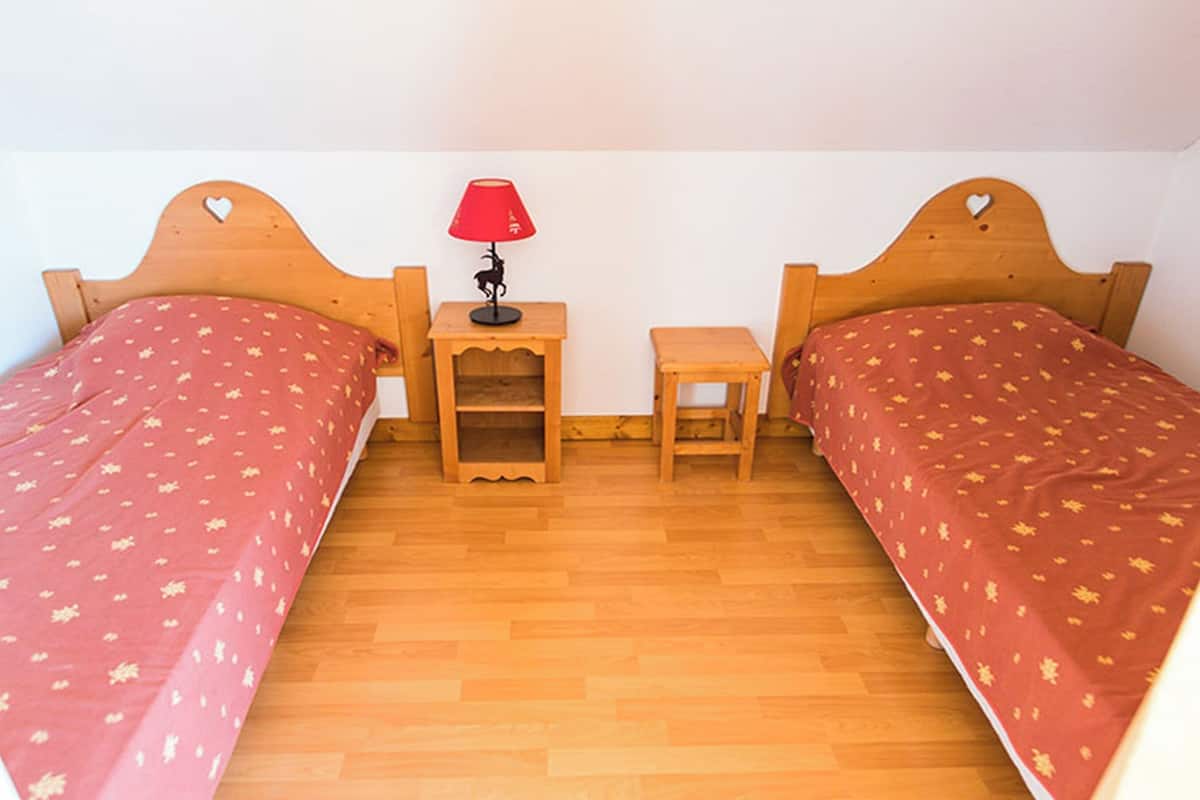 Une chambre avec deux lits en bois, une petite table avec une lampe et une table de chevet.