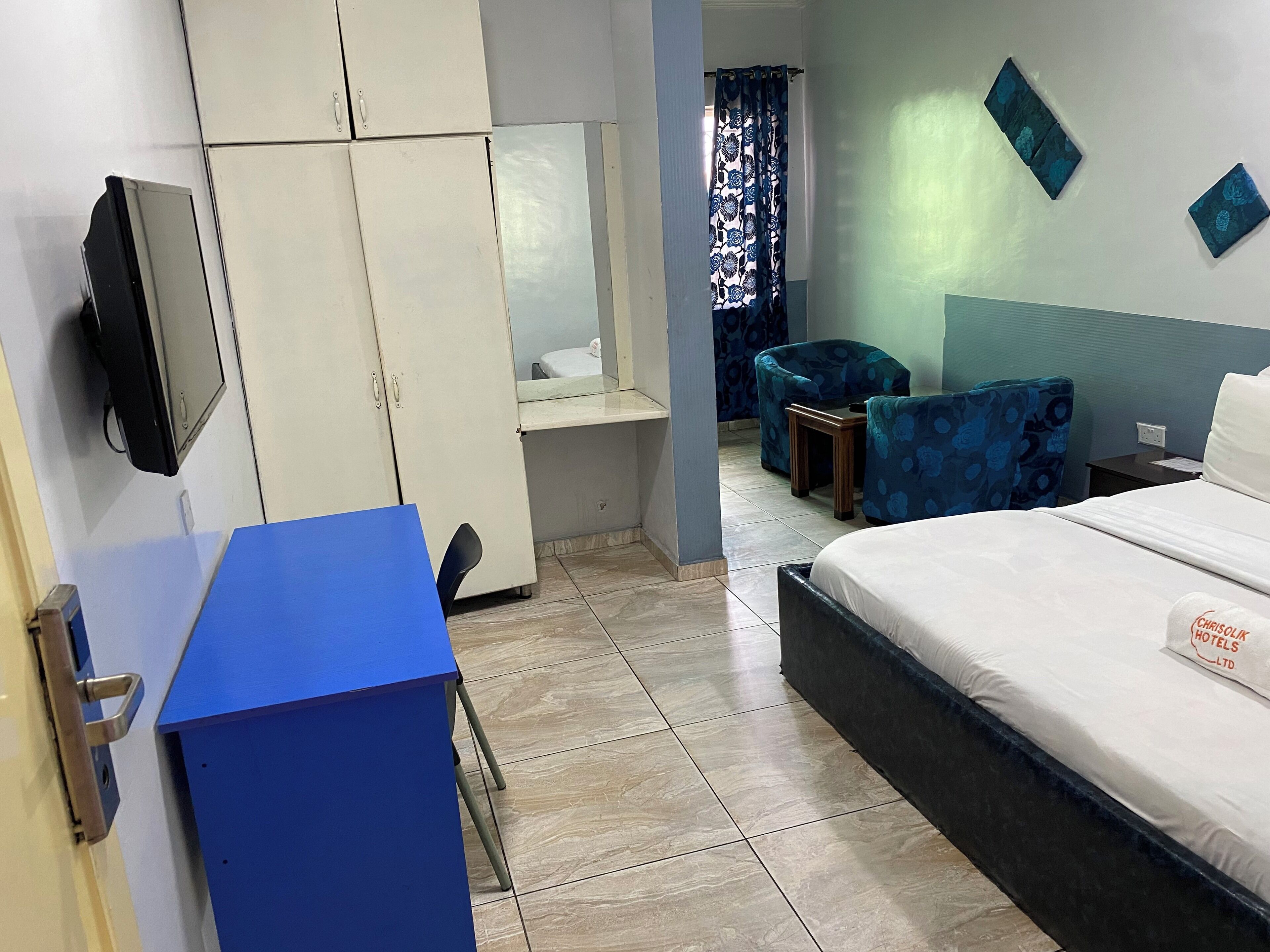 A hotel room with a bed, a desk, a wardrobe, and a chair.