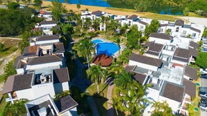 Vista aérea de una zona residencial con varias casas, una piscina y palmeras.