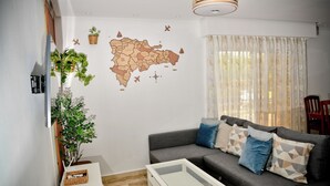 Una sala de estar con un sofá gris, una mesa de centro blanca, un adorno de pared con un mapa y una planta en maceta.