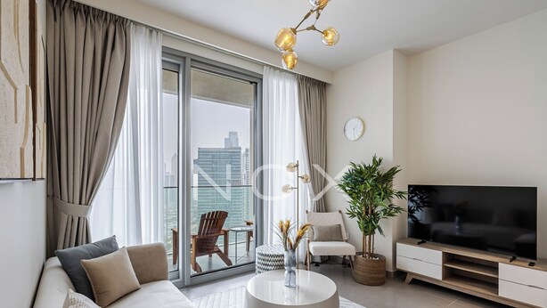 A modern living room with a sofa, a round coffee table, a TV, and a large window with curtains. - 1BR 2510 Forte T2 (Dubai)
