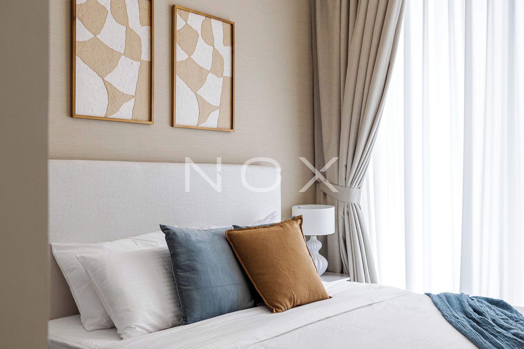 Une chambre d’hôtel moderne avec un grand lit, deux oreillers, une lampe de chevet et une œuvre d’art abstraite au mur.