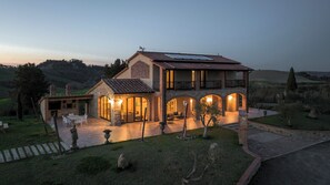 A two-story house with a stone facade, a balcony, and a well-lit patio area. - Villa TOSCA Private Home - Luxury Farm Stay with Restaurant and Experiences (Toscana)