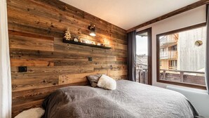 Un dormitori amb una paret de fusta, un llit amb llençol gris, un almofí blanc i esponjós, una petita prestatgeria amb objectes decoratius i una finestra amb vista a edificis.