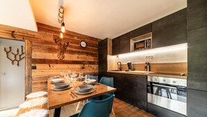 Una cuina moderna amb una paret de fusta, una taula de dinar preparada per a quatre persones i un forn de mur.