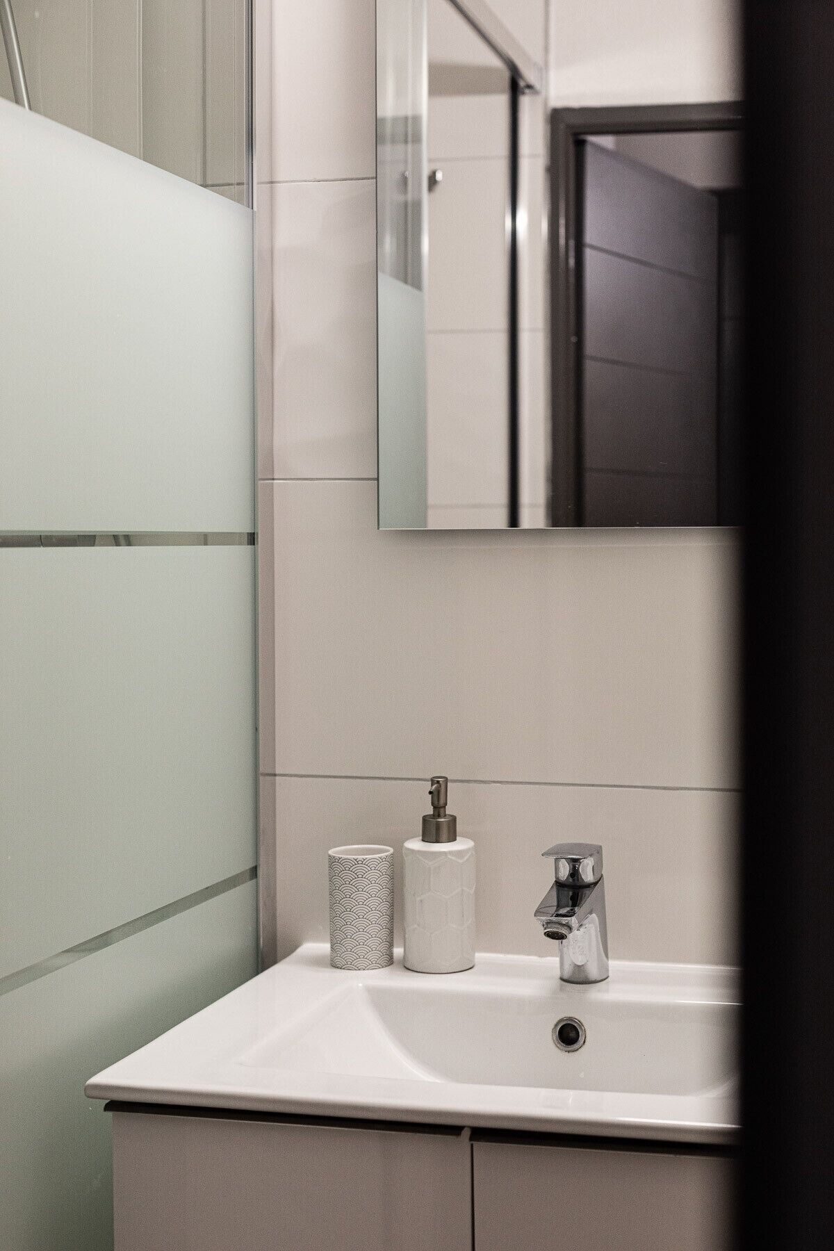 A bathroom with a white sink, a mirror, and two patterned containers.