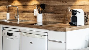 A compact kitchen with a wooden backsplash, a built-in dishwasher, a coffee machine, and a sink with a modern faucet. - La Yama - Immodreams - Avoriaz (Avoriaz)