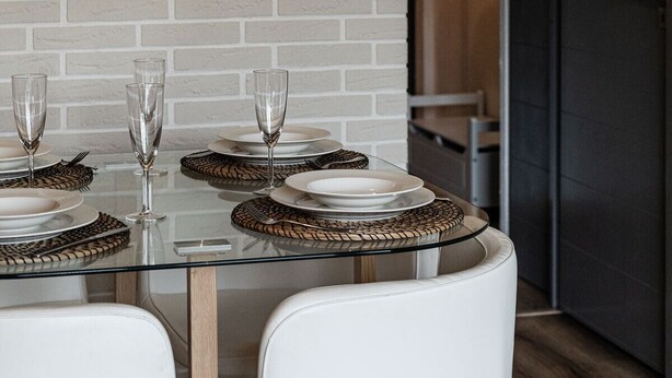 A modern dining area with a brick wall, a glass table set with plates, glasses, and woven placemats. - La Yama - Immodreams - Avoriaz (Avoriaz)