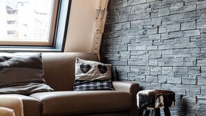 Een gezellige kamer met een bruine leren bank, een klein krukje en een houten vloer. Een raam met uitzicht op gebouwen is zichtbaar.