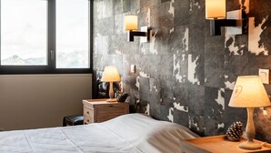 Un dormitorio con una cama grande, dos mesitas de noche con lámparas, una mesita auxiliar de madera y una pared con textura.