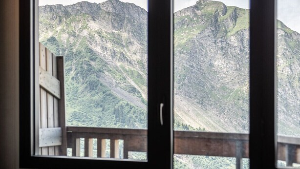 Una habitación con una mesa de comedor y sillas, una ventana que ofrece vistas a montañas y una baranda de madera en el exterior.