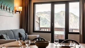 Un comedor con una mesa dispuesta para cuatro personas, un sofá y un amplio ventanal con vistas a la montaña.