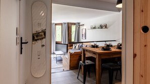 Ein gemütlicher Essbereich mit einem Holztisch, gedeckt für vier Personen, einer Bank mit Kissen und Blick auf einen Garten durch ein Fenster.